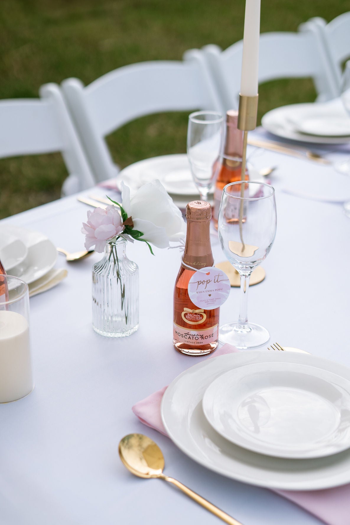Table setting with bottles, glasses, and plates on a white tablecloth outdoors.