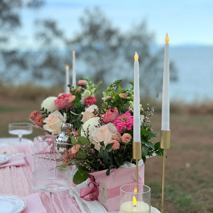 Decorative table setting with flowers, candles, and glasses outdoors.