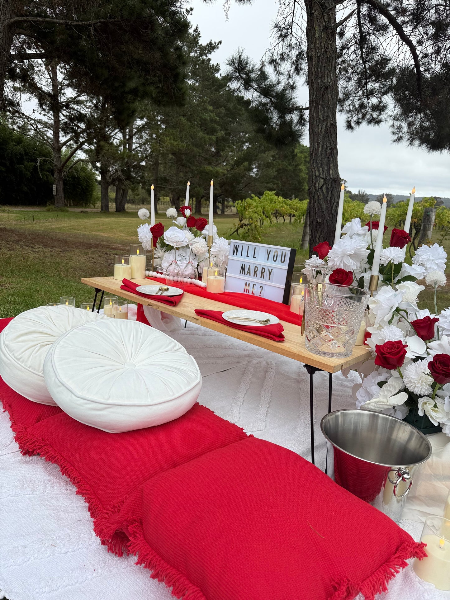 Red tablecloth with a white cushion and a table and floral arrangement in the background