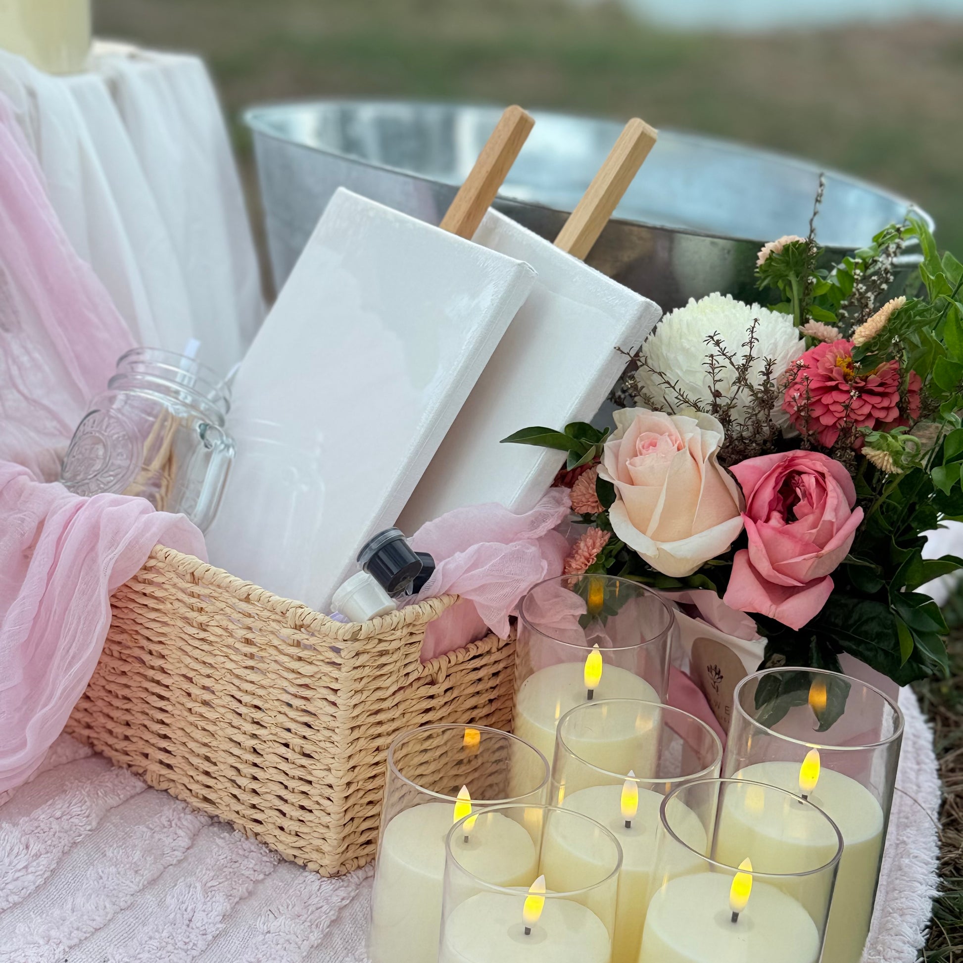 Outdoor setting with candles, flowers, and a basket on a blanket