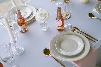 Elegant table setting with plates, glasses, and bottles on a white tablecloth.