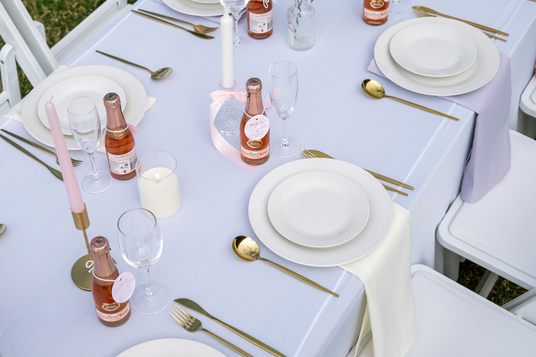 Elegant table setting with white tablecloth, gold cutlery, and pink candles.