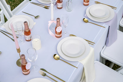 Elegant table setting with white tablecloth, gold cutlery, and pink candles.