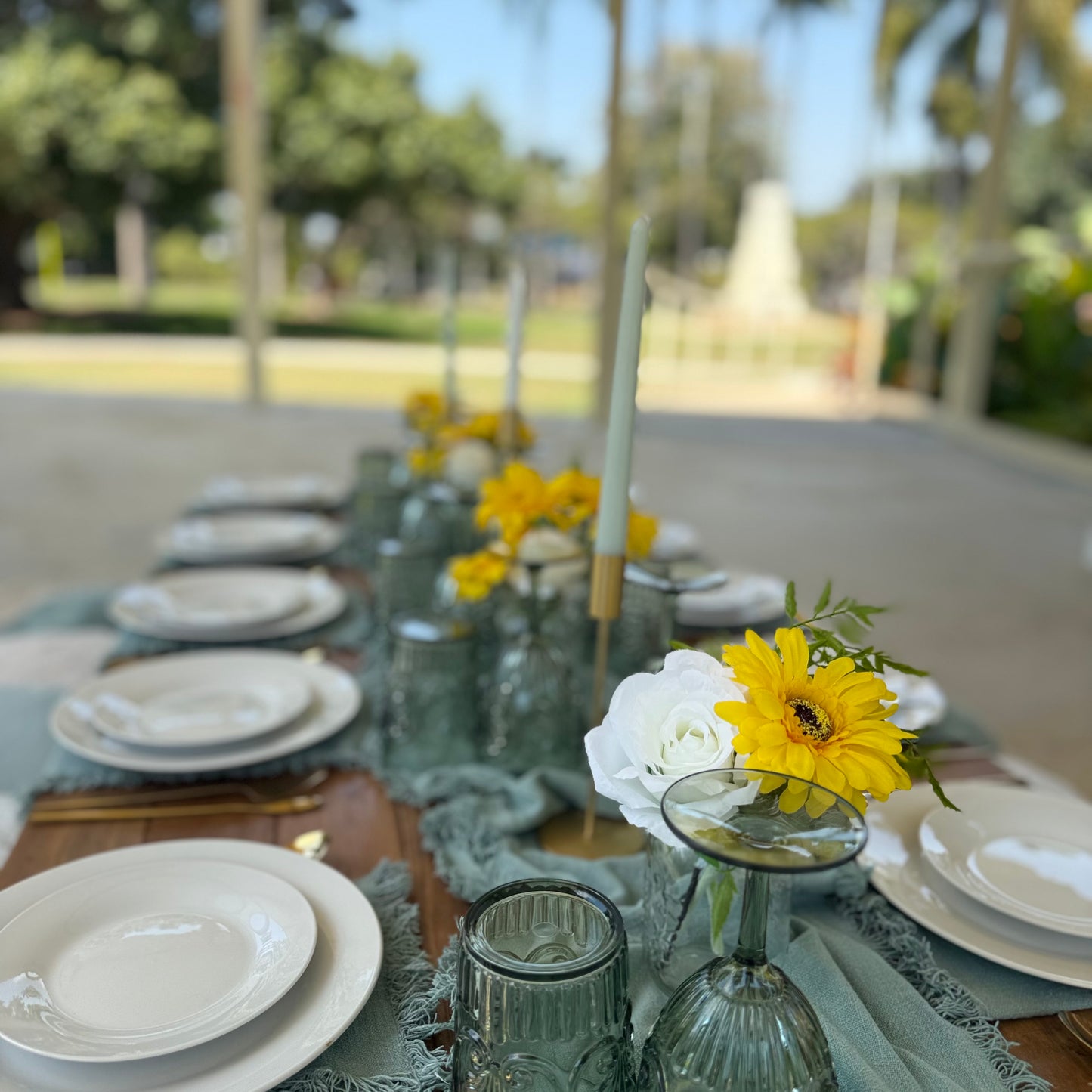 Dining table set with plates, glasses, and floral decorations outdoors.