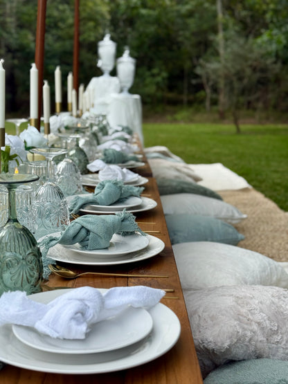 Long outdoor table set with white plates, green and white napkins, and decorative items on a grassy background.