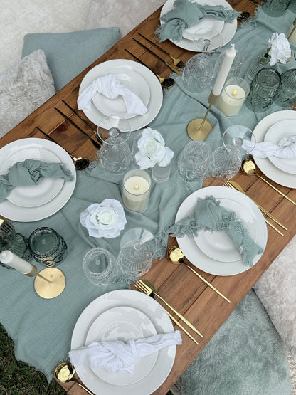 Elegant table setting with white plates, gold cutlery, and decorative flowers on a wooden table.