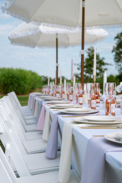 Outdoor dining setup with white chairs, tables, and umbrellas under a clear sky.