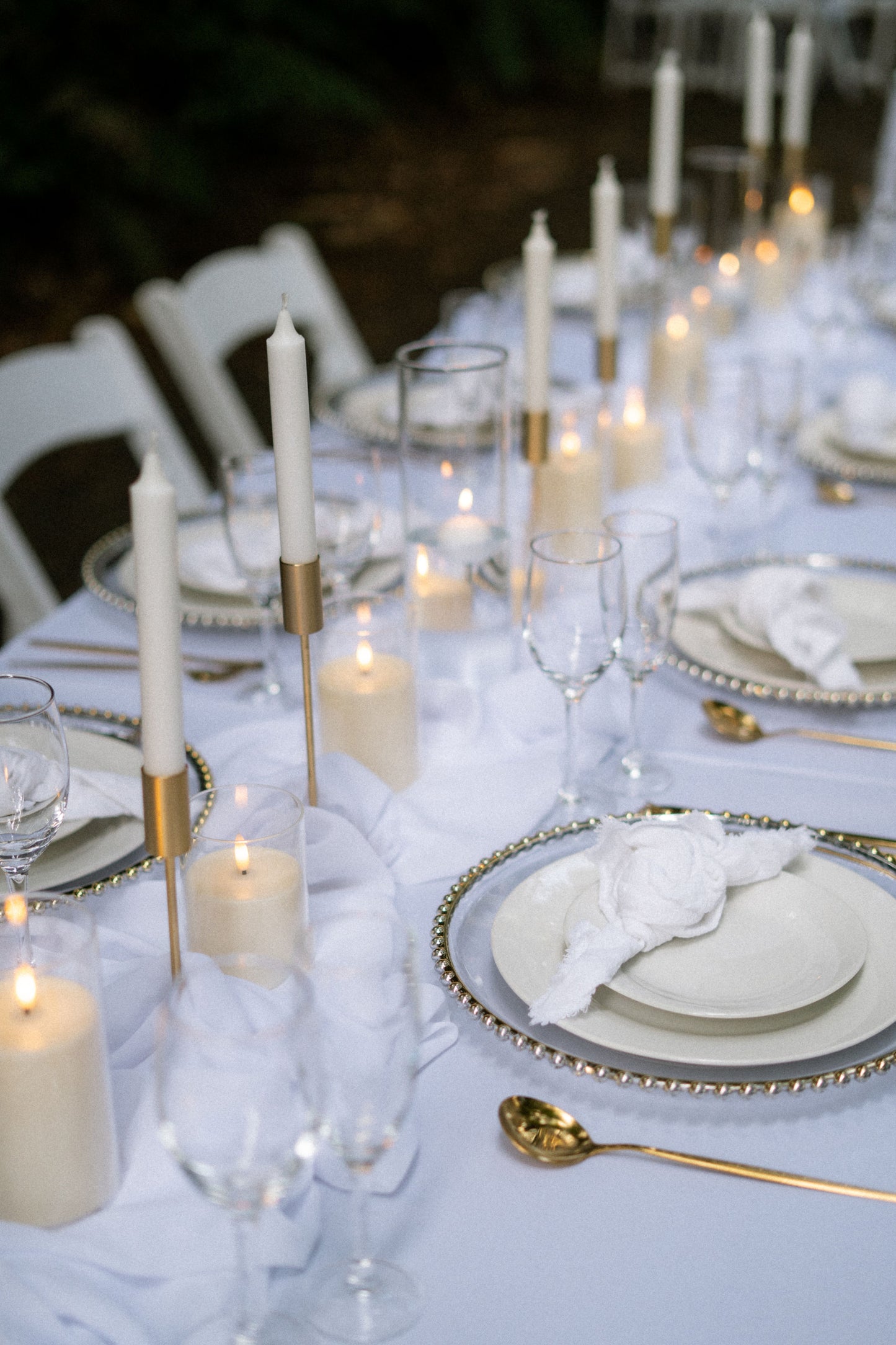 Elegant table setting with white candles, plates, and glasses on a white tablecloth.