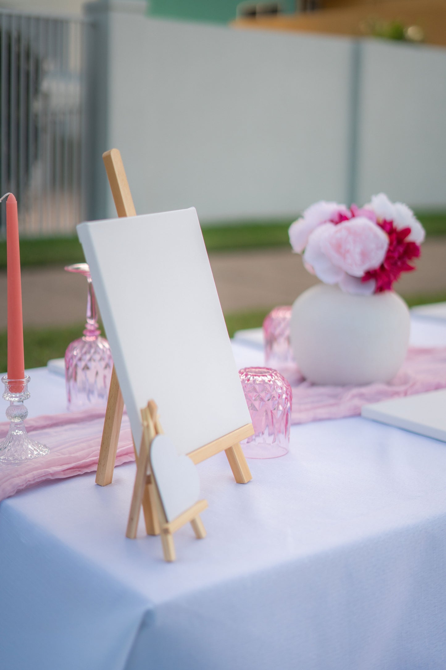 Small easel with a blank canvas on a table with pink flowers and candles.