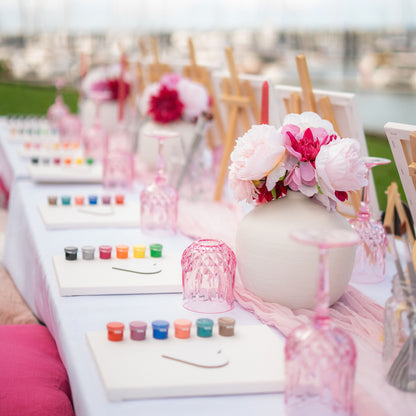 Decorated table with art supplies and flowers, sip and paint experience.